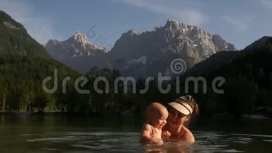 幸福的家庭<strong>妈妈</strong>和宝宝在一个温暖的山湖里游泳，背景是高高的雪山。 <strong>母亲<strong>节</strong></strong>`