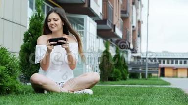 快乐美女在智能<strong>手机</strong>上<strong>玩手机</strong>游戏，坐在房子附近的草地上。