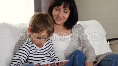 母亲和儿子<strong>一起</strong>坐在沙发上，用平板电脑<strong>看电影</strong>。 幸福的家庭，科技