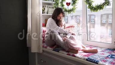 <strong>妈妈</strong>和女儿正坐在窗前的圣诞装饰背景上。 幸福的家庭<strong>妈妈</strong>和<strong>宝宝</strong>