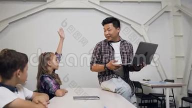 可爱的白种人女学生和同学坐在桌子后面，<strong>举手</strong>向韩国人<strong>提问</strong>
