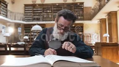 一个戴眼镜、戴胡子的人，在图书馆桌上看书