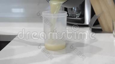 女人的手把牛奶白色的液体倒入一个塑料<strong>圆筒</strong>，放在白色的桌子<strong>上</strong>