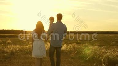 爸爸和<strong>妈妈</strong>带着她的小女儿在田野里的夕阳下抱着她的<strong>怀里</strong>散步。 家人和女儿一起玩