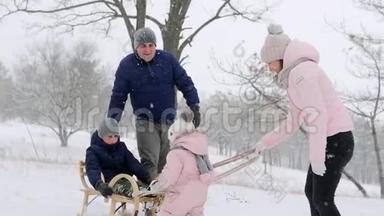 幸福的家庭在下雪的冬天滑雪。 女儿<strong>帮助父亲</strong>和母亲在下雪时和儿子拉雪橇。 男孩