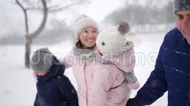 友好的全家人在降雪的情况下在冬天的森林里散步。 父亲、母亲、儿子和女儿