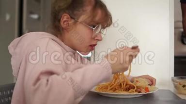 在学校食堂里吃意大利面条的少女。 健康饮食的女孩戴眼镜