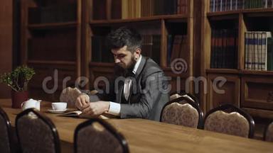 咖啡休息时间看书的人。穿着经典西装的男士坐在复古的室内、图书馆、书架上