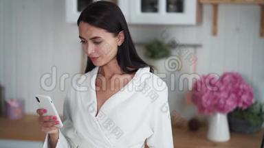 穿着白色浴袍的女人在手机上发信息，用手机在家工作