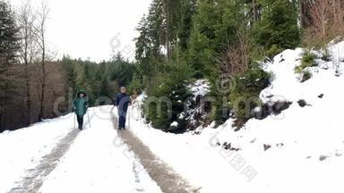一名中年妇女和一名身穿夹克衫的男子在冬季沿着一条带有北欧步行杆的森林道路行走，这是一种运动的概念，