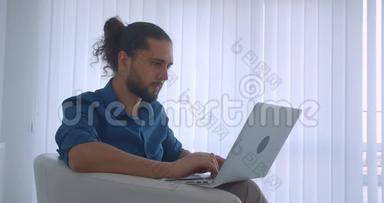 现代自由职业者在光办公室坐在扶手椅上的笔记本电脑上打字的照片<strong>变成</strong>了相机和微笑