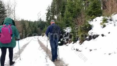 一名中年妇女和一名身穿夹克衫的男子在冬季沿着一<strong>条带</strong>有北欧步行杆的森林道路行走，这是一种运动的概念，