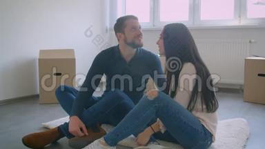 年轻的白种<strong>人</strong>夫妇正坐在靠近窗户的新房子的地板上，还<strong>有梦想</strong>着新家生活的纸盒。