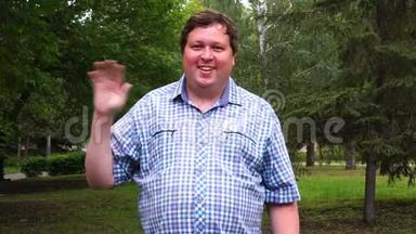 一位身穿格子衬衫的胖子在公园里用手愉快地敬礼
