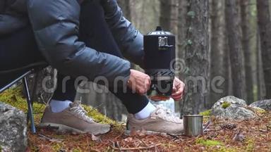 妇女使用燃气燃烧器在森林露营中温<strong>暖茶</strong>，在徒步旅行中休息。