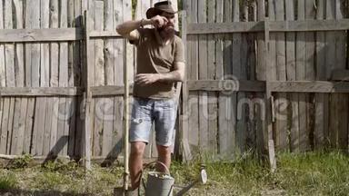 一幅长胡子的农夫的全身画像，他拿着铲子，在一个木制操场上的农场里玩得很开心。 生态农场。 希普斯特农民
