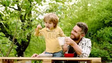 夏园晚会爸爸带儿子.. 快乐的父亲和他的儿子坐在桌子上吃着健康的食物，带着有趣的味道