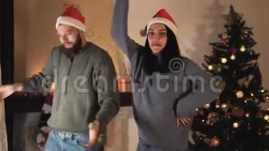 有趣的年轻夫妇戴着圣诞帽在<strong>圣诞树</strong>前的房间里跳舞<strong>和</strong>跳跃。 男人<strong>和女孩</strong>