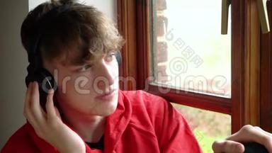 青少年男子坐在窗边听无线蓝牙耳机音乐