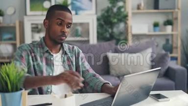 美国黑人自由职业者用笔记本电脑打字，然后摸着头感到疲倦和不快乐