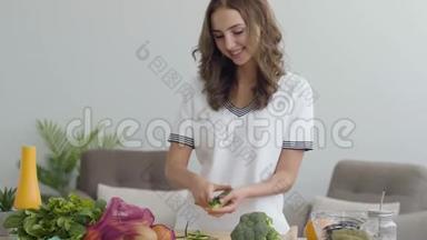 可爱的女孩用刀切黄瓜，而站在厨房的一张桌子在家里。 熟练的厨师准备早餐