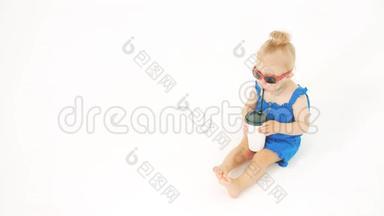 戴墨镜的小女孩在白色背景上用吸管从纸杯里喝饮料