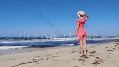 年轻迷人的女人拿着她的帽子，穿着红色的裙子看着暴风雨的大海和地平线。 红色的裙子在w上拍<strong>打</strong>