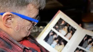 高加索族的老人，戴着蓝色的眼镜，带着照片翻阅相册，坐着。 记忆和概念