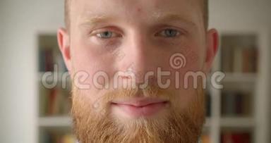 红发胡子白种人男学生的特写肖像，脸上洋溢着笑容，开心地看着图书馆里的摄像机