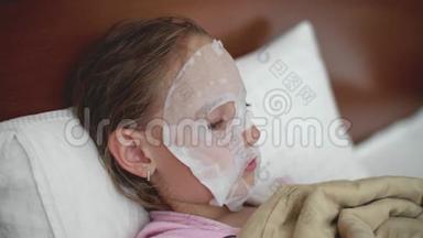青春期前的女孩用布保湿<strong>面膜敷</strong>脸躺在床上..