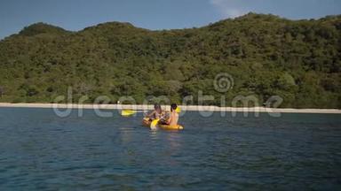 一对朋友在蔚蓝的海洋湾附近的一个野生热带岛屿慢动作皮划艇，享受娱<strong>乐运动</strong>