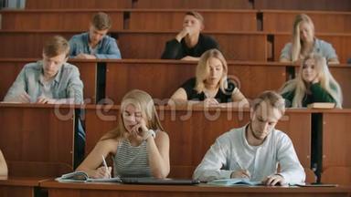 现代学生，男人和女人，坐在一个大教室的<strong>课桌</strong>前，写一篇讲稿。