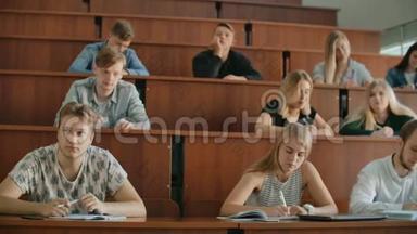 在课堂上，多民族学生听讲师，在笔记本上写作。 聪明的年轻人在