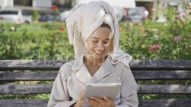 一幅身着浴袍、头戴毛巾、坐在公园长椅上查看资料的微笑年轻女子的画像