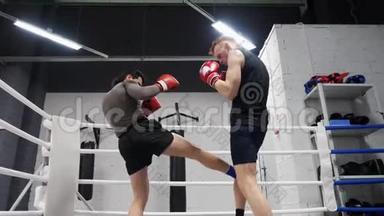 两个拳击手在拳击场上训练双腿踢。 低角度视角。 拳击手和私人教练一起训练健身房