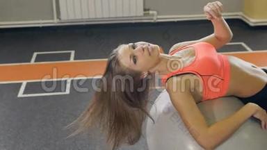 健身房里的健身女人靠普拉提球休息。 年轻女子在健身球上做运动。 年轻女孩的粉色健身