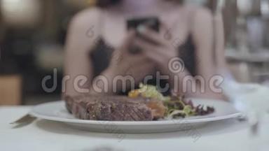 美味的牛排，蔬菜和<strong>叶子</strong>躺在盘子里，在餐厅的女人面前。 `<strong>女士</strong>的手在发短信