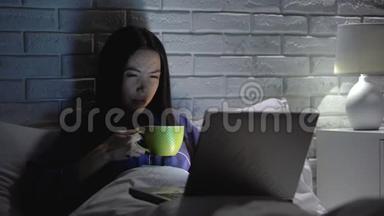 亚洲女人在卧室里工作，在笔记本电脑上喝咖啡，最后期限