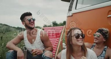 一群朋友在野餐时坐在野餐椅上，坐在一辆复古的面包车后面，微笑着交谈。