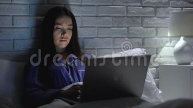 睡眠不足的女人晚上在床上用笔记本电脑工作，在无聊的项目中没有动力