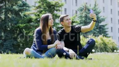 快乐的年轻夫妇通过手机在视频聊天，坐在公园的草地上，通过视频与朋友交谈