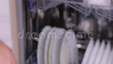男人`手正在用肮脏的白色盘子关闭洗碗机。