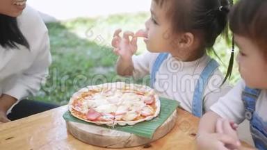 可爱的饥饿的女孩喜欢在后院和妈妈一起吃自制的披萨。 有家人的小女孩在户外的午餐桌上。