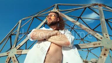 英俊的留胡子的旅行男子在蓝天海滩背景下在网格附近摆姿势放松户外