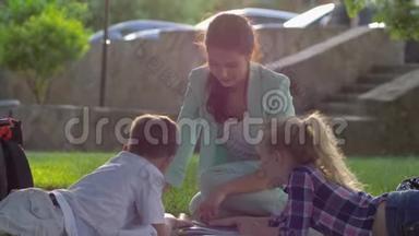 在户外<strong>看书</strong>，快乐的女家庭教师为小<strong>男孩</strong>和小女孩在阳光明媚的露天草地上坐着<strong>看书</strong>