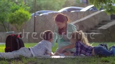 开朗的女教育家<strong>为</strong>小<strong>男孩</strong>和小<strong>女孩</strong>在阳光明媚的阳光下坐在大自然的绿草上读书