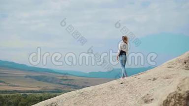 一个金发女孩站在一座山的顶上，背景是湛蓝的天空，她用手机举起了手