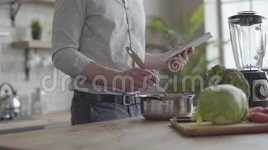 不可辨认的男人在衬衫上煮汤，检查食谱在厨房里的平板电脑上。 健康观念