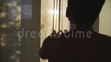 无法辨认的运动男在酒店的卧室<strong>拉开</strong>窗帘，早上看着窗外。 年轻人