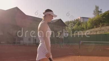 年轻漂亮的女孩打网球。 一个穿着白色运动服的女人专门训练网球。 年轻漂亮的女孩